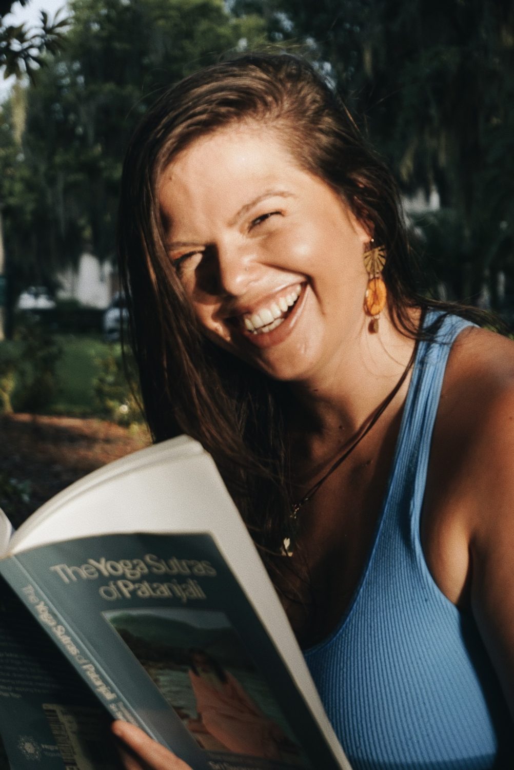 Mandy laughing over an open book beneath mossy trees
