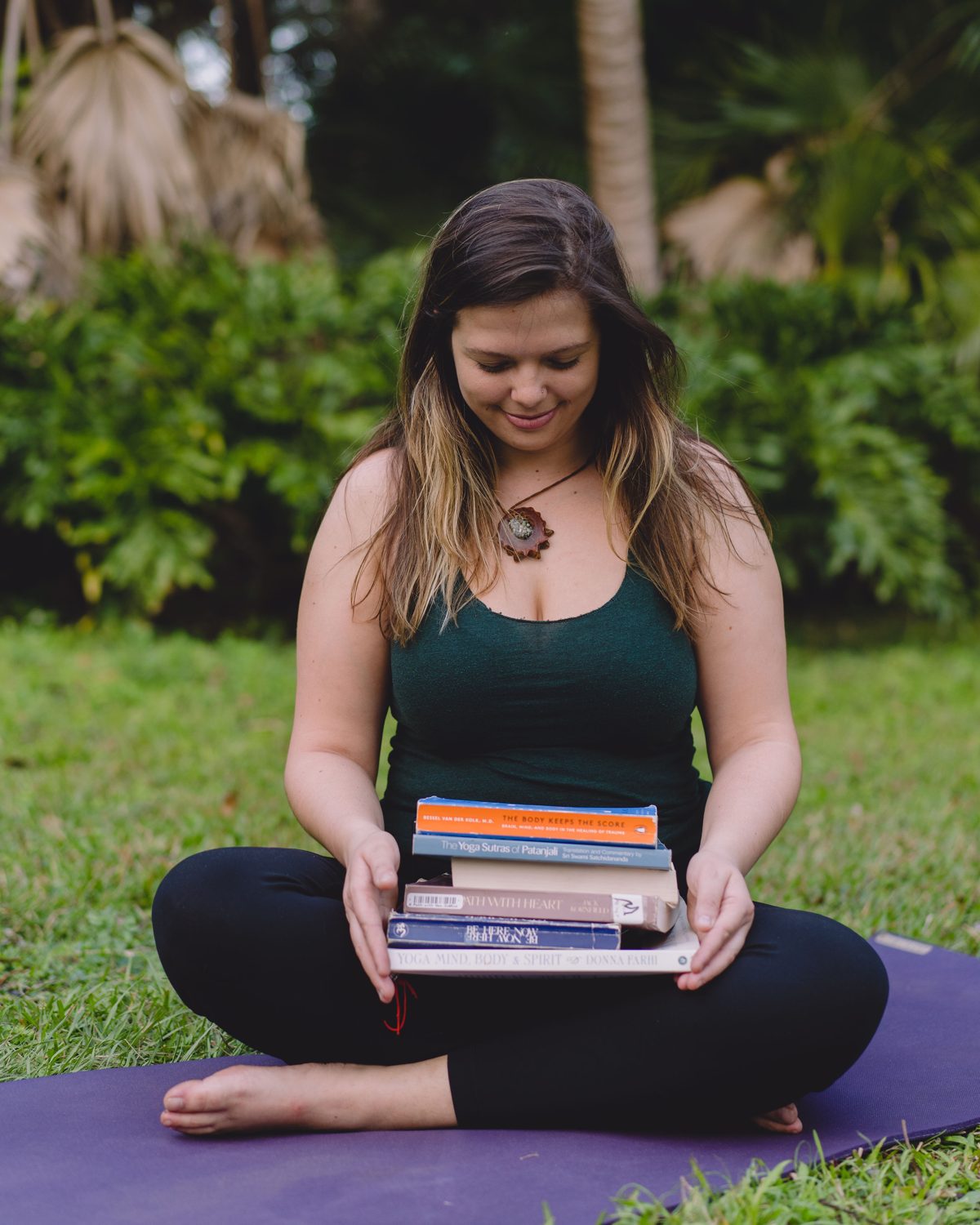 Mandy Roux seated on a yoga mat holding the books that shaped her somatic therapy practice