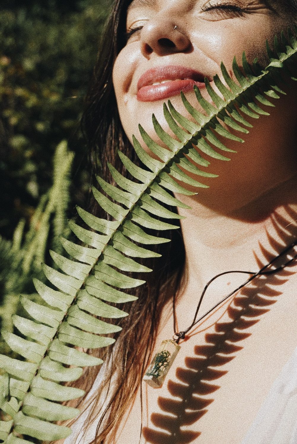 Mandy Roux, somatic counselor in Orlando, face turned to the sunlight behind a green fern frond