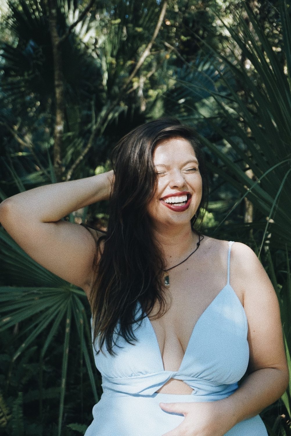 Mandy Roux, somatic therapist in Orlando Florida offering online therapy, laughing in a pale blue dress among green palms