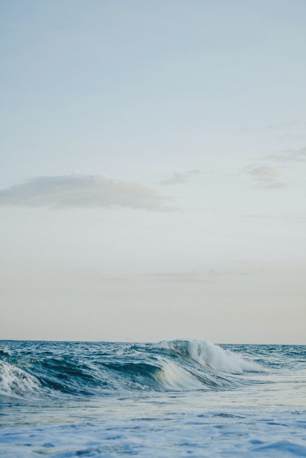 A turquoise ocean wave rolling toward shore under a soft sky