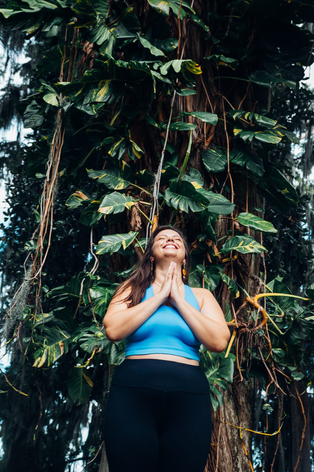 Mandy with hands at heart center beneath hanging vines, grounded in her body