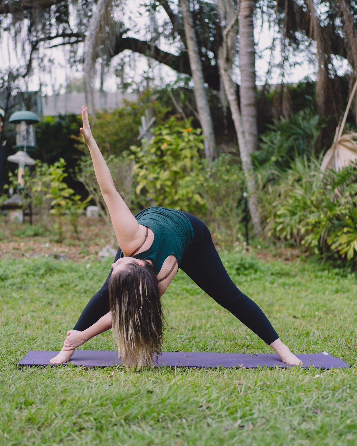 Somatic therapy in Florida, Mandy folding into a wide legged yoga stretch in a green garden